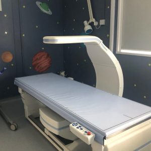 Paediatric DXA Scanner: "A DXA bone density scanner bed in a hospital room decorated with a space-themed ceiling