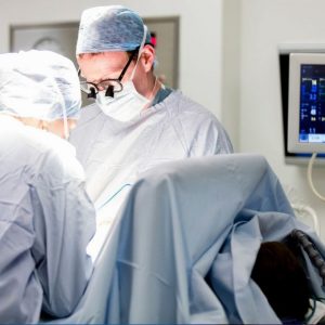 Operating Microscope for CHI at Crumlin: A surgeon in a mask, cap and gown looking down through surgical equipment in an operating theatre