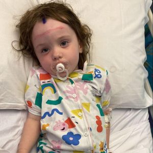 Girl in Peppa Pig pyjamas resting in her hospital bed with a soother.