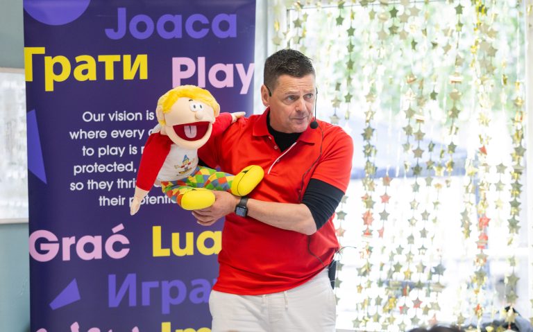 A play worker with a puppet beside a colourful play area display