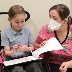 Hallie-300x300: "Hallie with a healthcare worker in a mask during a hospital activity.