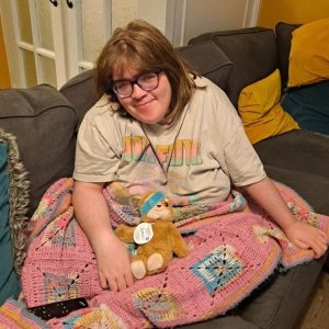 Patient Emer: "Emer smiling on a couch wrapped in a blanket."