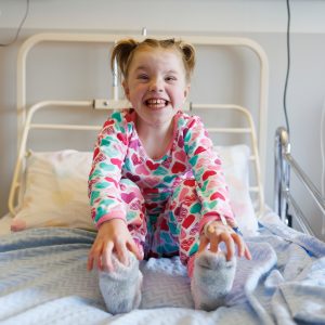 Patient Jessica: "Jessica smiling in her hospital bed wearing colourful pyjamas."